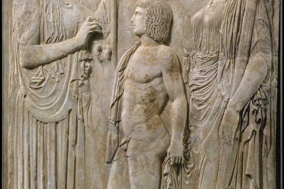 Three draped classical figures carved in high relief on a marble panel, weathered to a warm off-white.